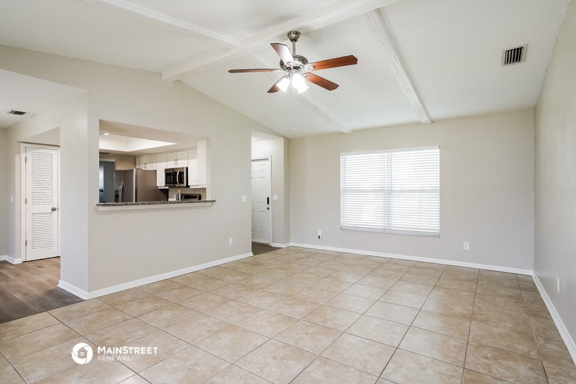 an empty living room with a ceiling fan and a kitchen