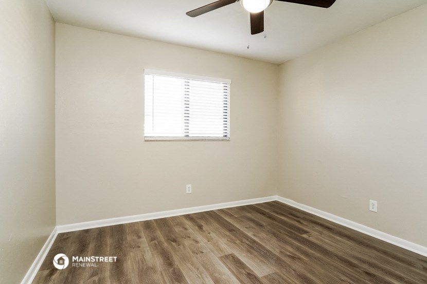 the spacious living room with wood flooring and a ceiling fan