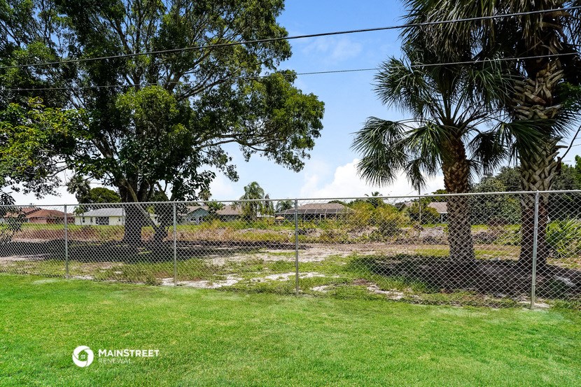 a yard behind a chain link fence with a dirt field and palm trees