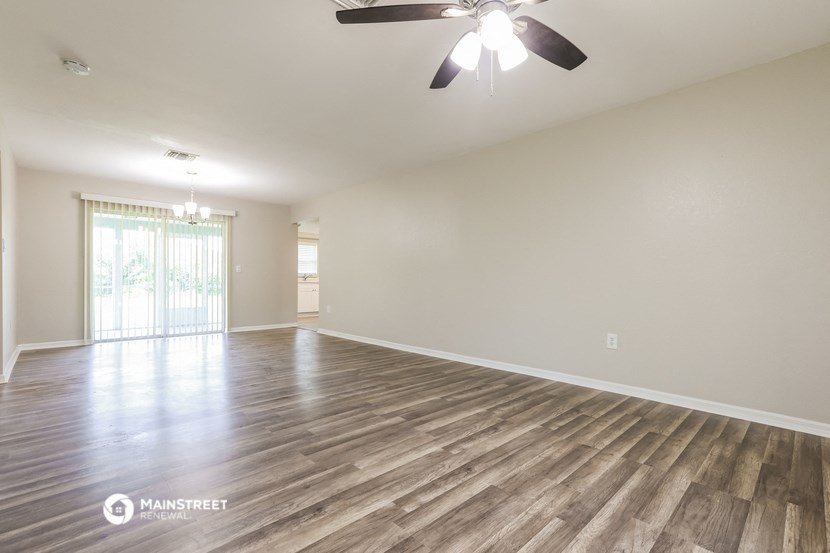 the spacious living room with wood flooring and a ceiling fan