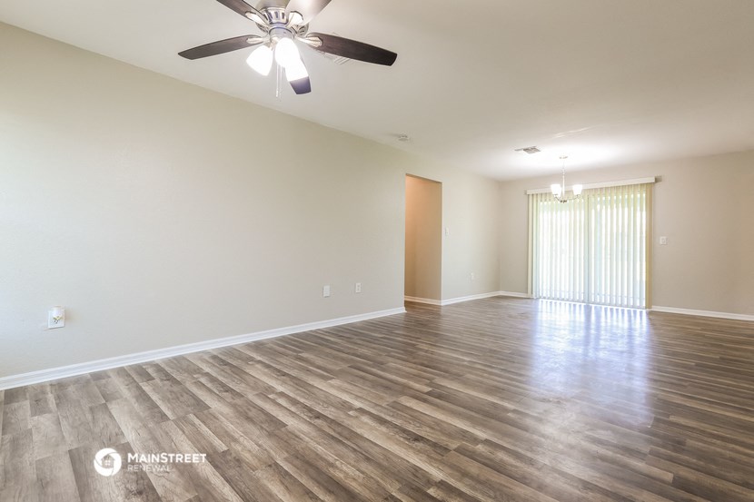 the spacious living room with wood flooring and a ceiling fan