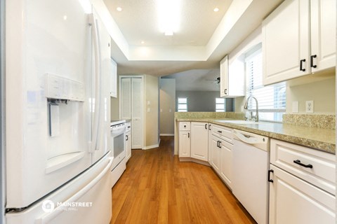 a kitchen with white cabinets and white appliances and wood floors