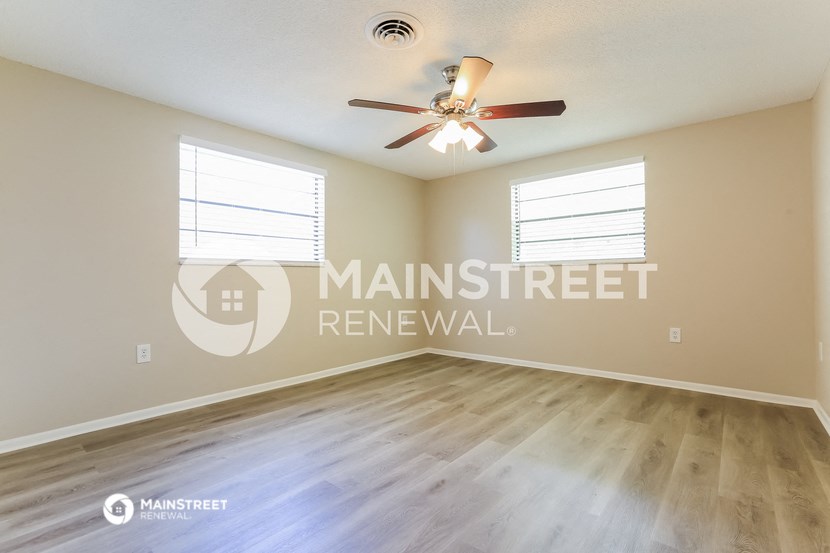 an empty living room with a ceiling fan and two windows