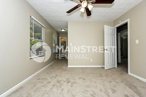 a spacious living room with beige carpet and a ceiling fan