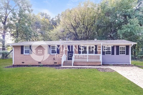 a small brick house with a white porch and a lawn