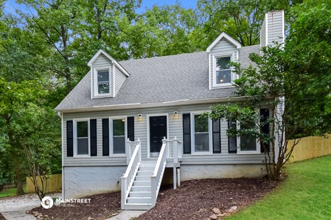 a small white house with white stairs and a yard with trees