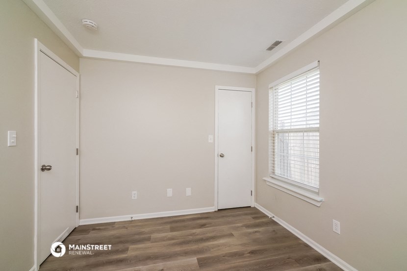a bedroom with white walls and wood flooring and a window