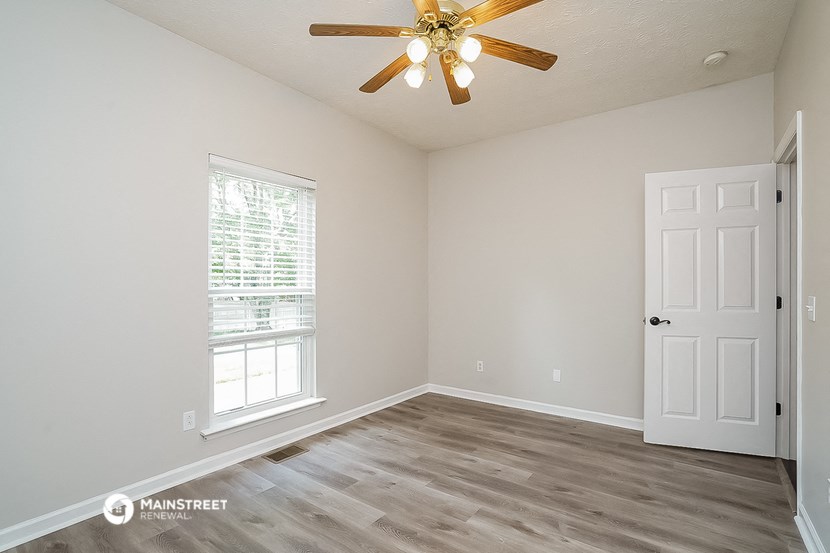 the spacious living room with white walls and a ceiling fan