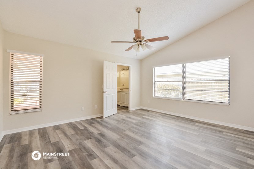 the spacious living room with a ceiling fan and a door to the bathroom