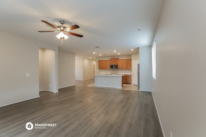 an empty living room with a ceiling fan and a kitchen