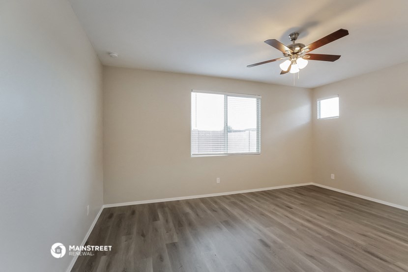 the spacious living room with wood floors and a ceiling fan