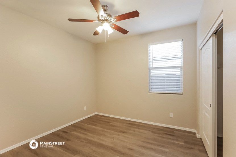 the spacious bedroom has a ceiling fan and hardwood flooring
