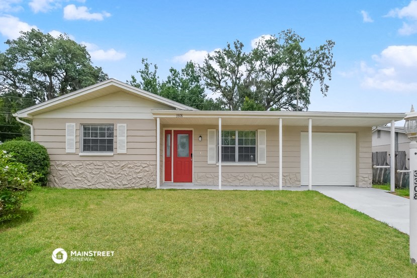 a small tan house with a red door and a lawn