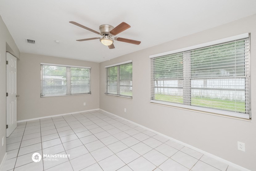 an empty living room with a ceiling fan and three windows
