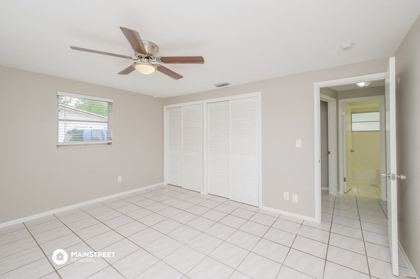 an empty living room with a ceiling fan and a door to a hallway