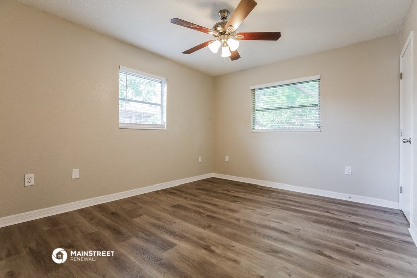 the spacious living room with hardwood floors and a ceiling fan
