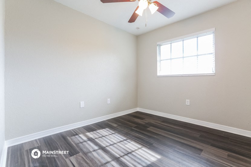 the spacious living room with wood flooring and a ceiling fan
