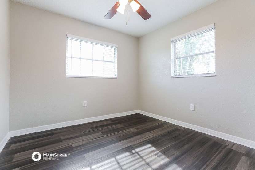 the spacious living room of an empty house with a ceiling fan and two windows