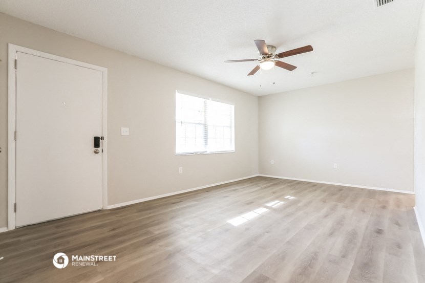 the spacious living room with hardwood floors and a ceiling fan