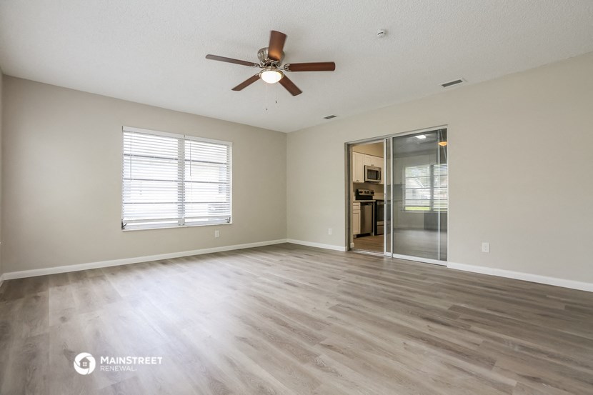 the spacious living room with hardwood flooring and a ceiling fan