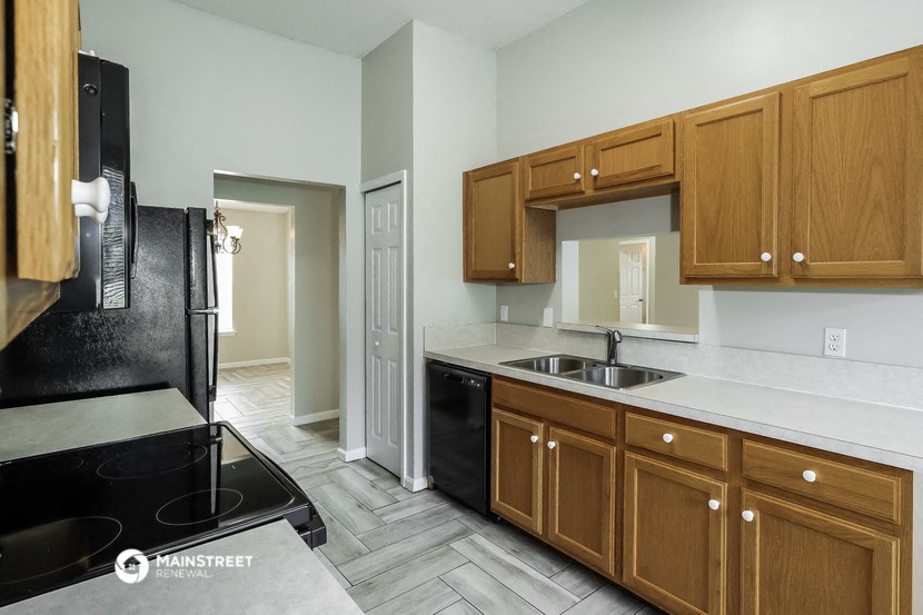 a kitchen with wooden cabinets and black appliances and a door to a hallway