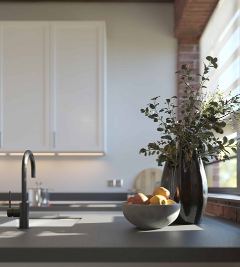 A kitchen counter with a bowl of fruit and a vase of greenery.