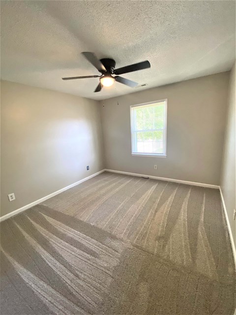 an empty living room with a ceiling fan and a window