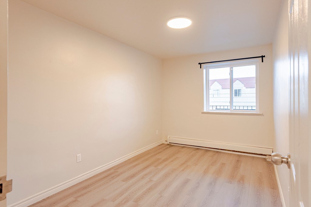 an empty bedroom with wood floors and a window