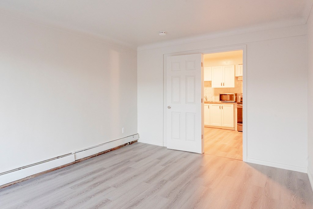 a living room with white walls and a door to a kitchen