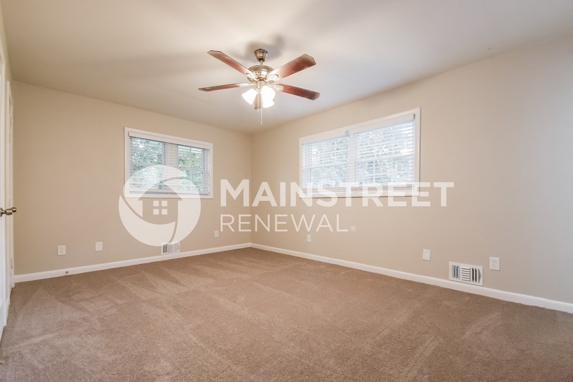 the spacious living room of a home with carpet and a ceiling fan