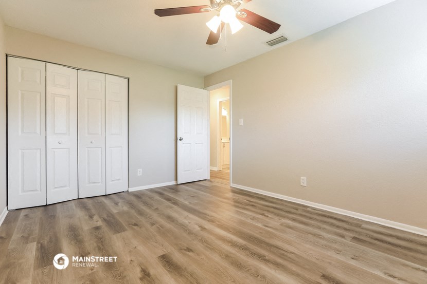 the spacious living room with white walls and a ceiling fan
