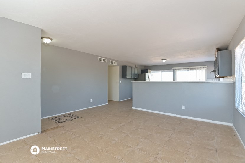 an empty living room with a kitchen and a tiled floor