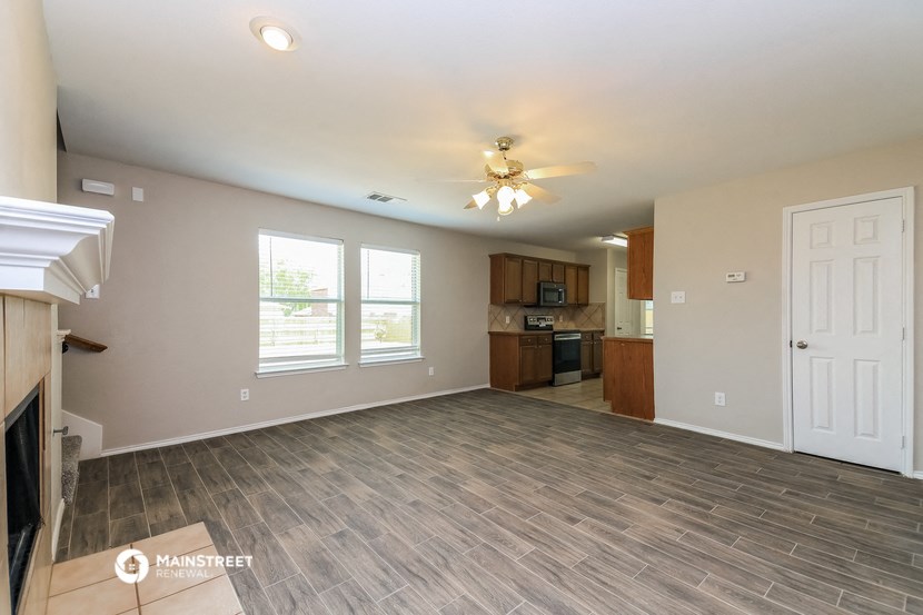 an empty living room with a kitchen and a ceiling fan
