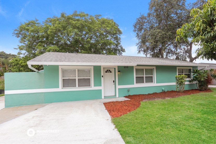 a blue and green house with a lawn and trees