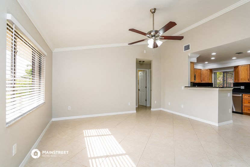 an empty living room with a ceiling fan and a kitchen