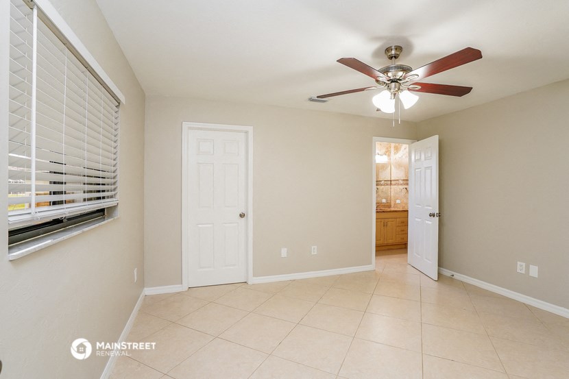 an empty living room with a ceiling fan and a door to a bathroom