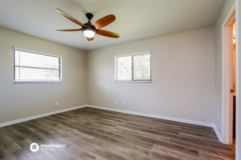 the spacious living room with wood flooring and a ceiling fan