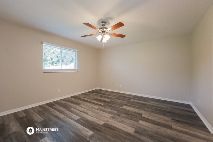 the spacious living room with wood flooring and a ceiling fan
