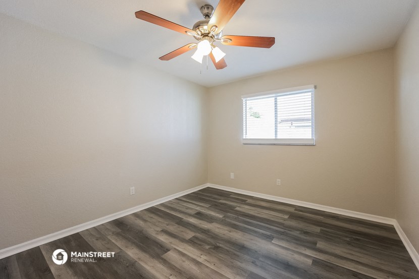 the spacious living room with wood flooring and a ceiling fan