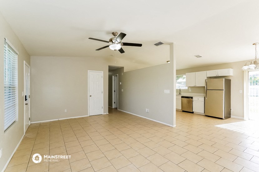 an empty living room with a ceiling fan and a kitchen