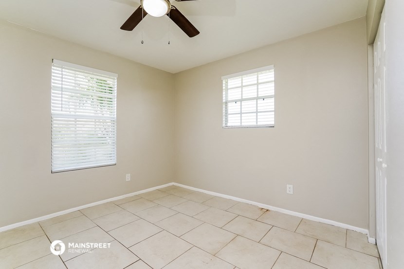 an empty living room with a ceiling fan and two windows