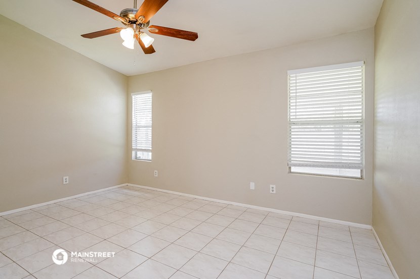the spacious living room has a ceiling fan and tiled floors