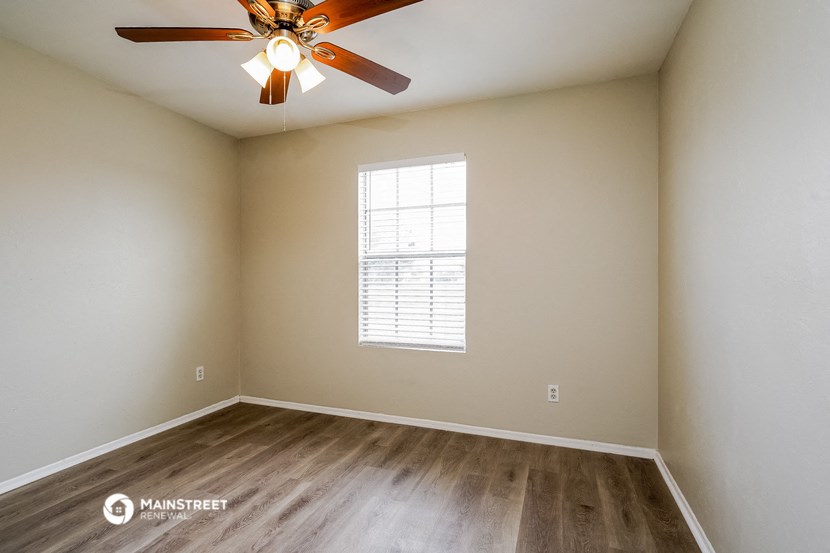 the spacious living room with wood flooring and a ceiling fan