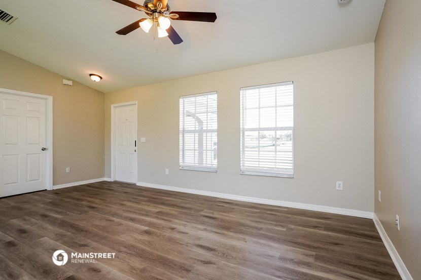 the spacious living room with a ceiling fan and two windows