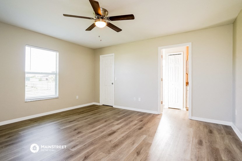 the spacious living room with hardwood flooring and a ceiling fan