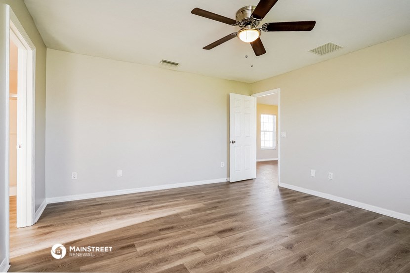 the spacious living room with wood flooring and a ceiling fan