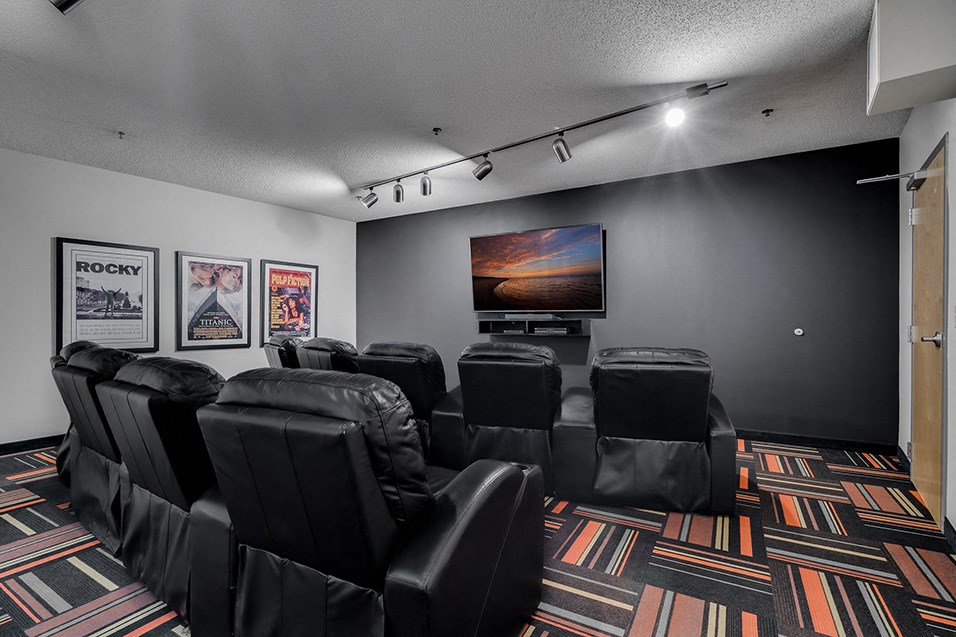 a theater room with black leather chairs and a flat screen tv