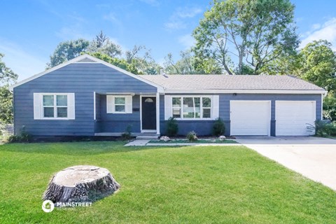 a blue house with a lawn and a tree stump in front