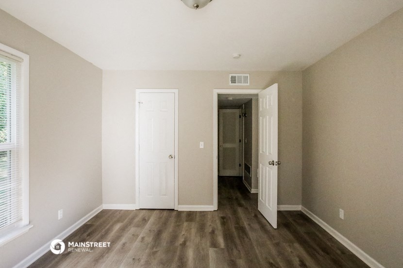 a bedroom with white walls and wooden floors and a door to a hallway
