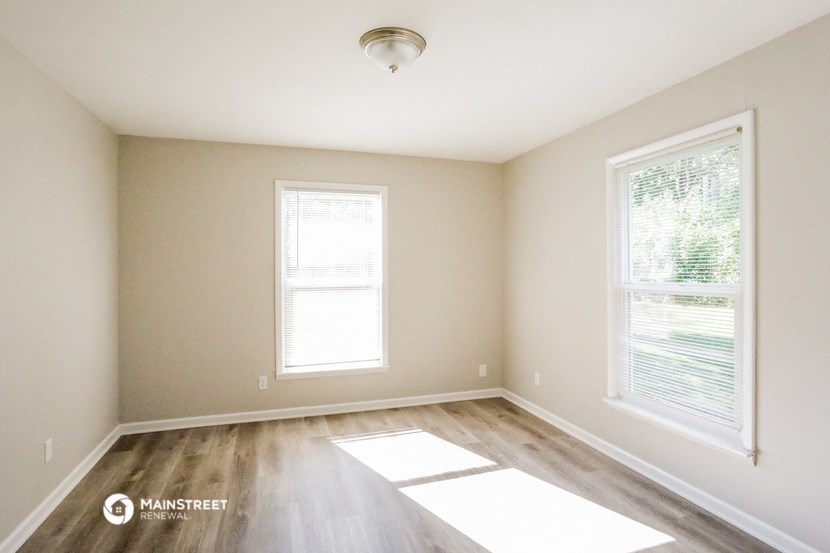 an empty room with wood floors and two windows